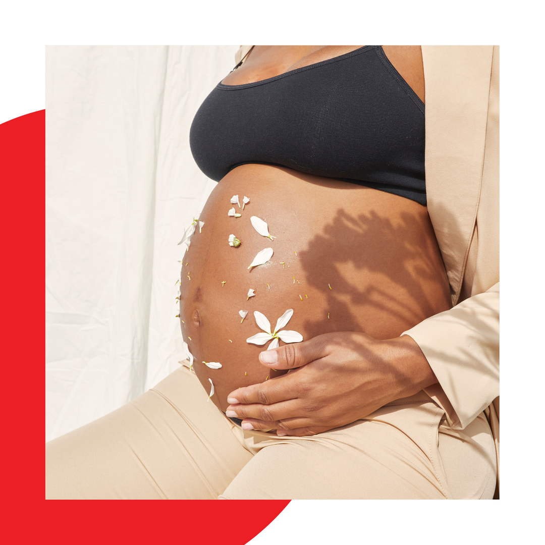 Pregnant belly shown decorated with petals in sunlight. 