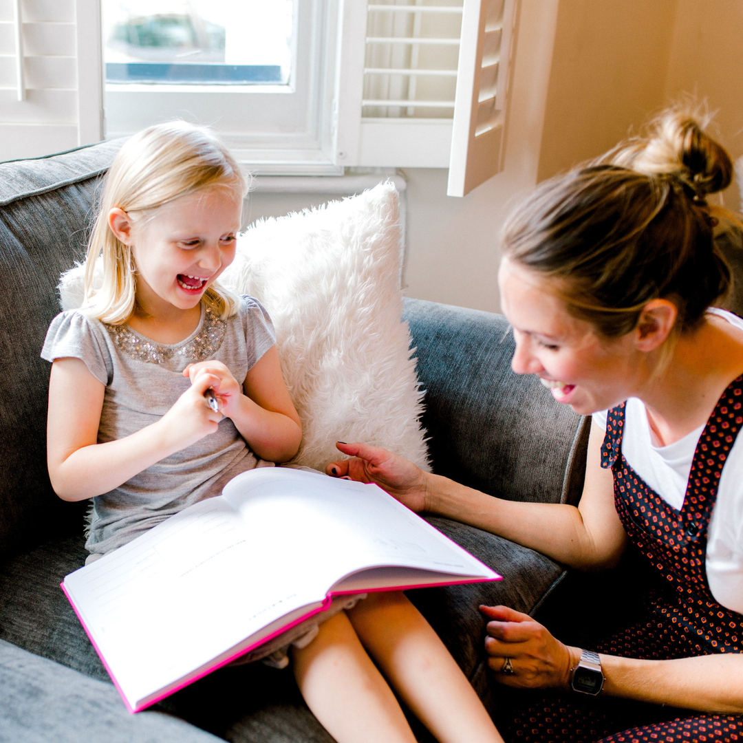 Mother and daughter sharing a happy smile together over an open copy of The Book of You