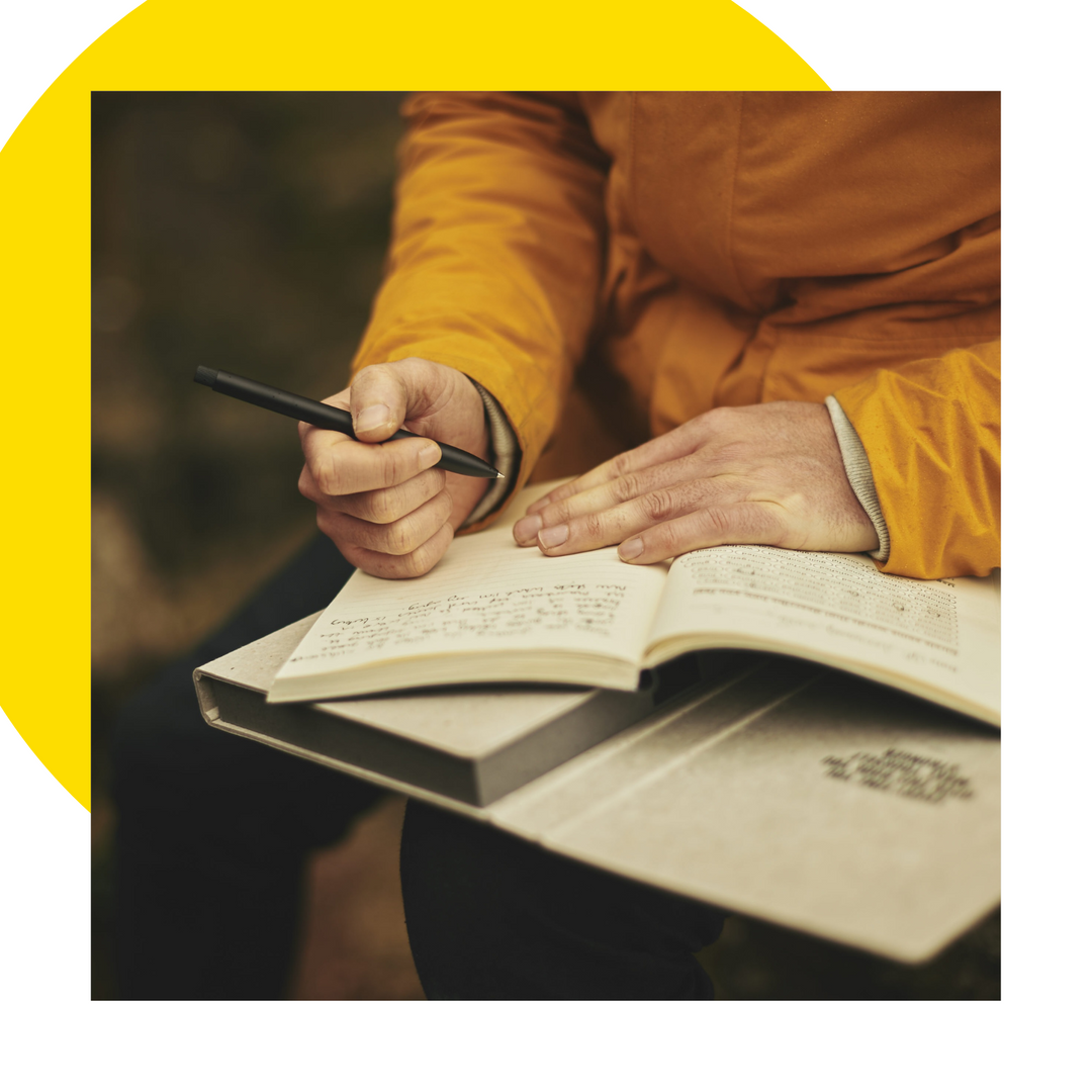 Hands holding pen and writing in journal.