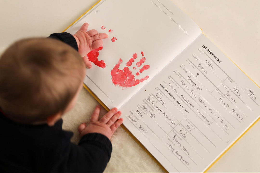 Baby adds painted handprints to their baby memory book on their first birthday
