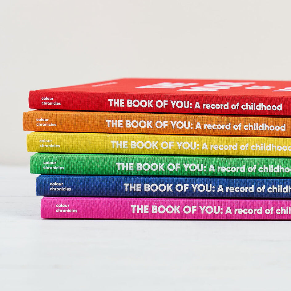 Baby gift of modern childhood journal shown stacked in six bright rainbow colours